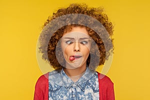 Closeup portrait of crazy woman with fluffy curly hair demonstrating tongue out and making silly face with crossed eyes