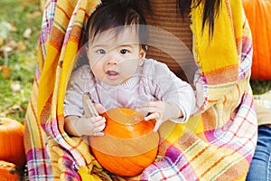 Closeup portrait of cute adorable funny Asian Chinese baby girl sitting in autumn fall park outdoor with yellow orange pumpkin