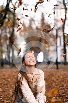 Closeup portrait of cute adorable smiling little Caucasian girl child playing with dry leaves standing in autumn fall