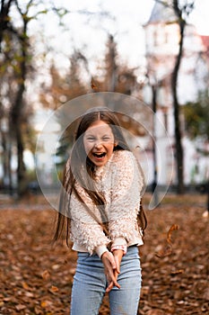 Closeup portrait of cute adorable smiling little Caucasian girl child playing with dry leaves standing in autumn fall