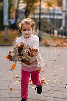 Closeup portrait of cute adorable smiling little Caucasian girl child playing with dry leaves standing in autumn fall