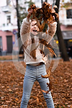 Closeup portrait of cute adorable smiling little Caucasian girl child playing with dry leaves standing in autumn fall