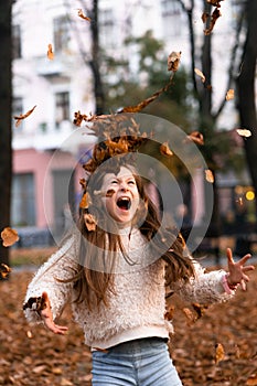 Closeup portrait of cute adorable smiling little Caucasian girl child playing with dry leaves standing in autumn fall