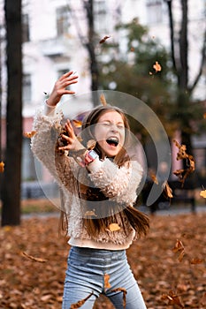 Closeup portrait of cute adorable smiling little Caucasian girl child playing with dry leaves standing in autumn fall