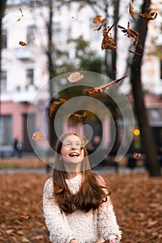 Closeup portrait of cute adorable smiling little Caucasian girl child playing with dry leaves standing in autumn fall