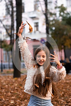 Closeup portrait of cute adorable smiling little Caucasian girl child playing with dry leaves standing in autumn fall