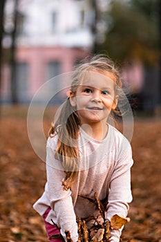 Closeup portrait of cute adorable smiling little Caucasian girl child playing with dry leaves standing in autumn fall