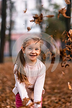 Closeup portrait of cute adorable smiling little Caucasian girl child playing with dry leaves standing in autumn fall