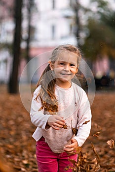 Closeup portrait of cute adorable smiling little Caucasian girl child playing with dry leaves standing in autumn fall