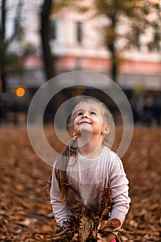 Closeup portrait of cute adorable smiling little Caucasian girl child playing with dry leaves standing in autumn fall