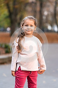 Closeup portrait of cute adorable smiling little Caucasian girl child standing in autumn fall park outside, looking in