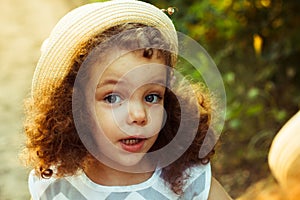 Closeup portrait of cute adorable smiling little curly haired Caucasian girl child standing in autumn fall park outside, looking i