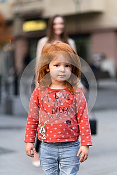 Closeup portrait of cute adorable smiling little red-haired Caucasian girl child standing in autumn fall park outside