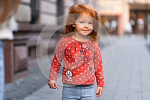 Closeup portrait of cute adorable smiling little red-haired Caucasian girl child standing in autumn fall park outside