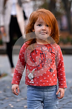 Closeup portrait of cute adorable smiling little red-haired Caucasian girl child standing in autumn fall park outside