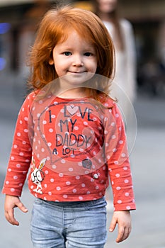 Closeup portrait of cute adorable smiling little red-haired Caucasian girl child standing in autumn fall park outside