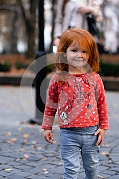 Closeup portrait of cute adorable smiling little red-haired Caucasian girl child standing in autumn fall park outside