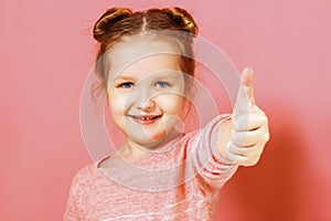 Closeup portrait of a cute attractive little child girl showing thumb up over pink background