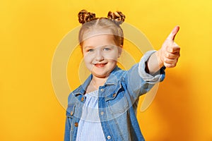 Closeup portrait of a cute attractive little child girl showing thumb up on yellow background