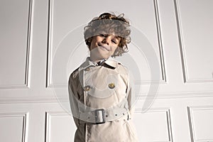 Closeup portrait of a cute curly little boy looking at camera, in stylish coat, isolated on a white background