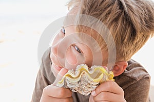 Funny tanned boy holding happily yellow sea shell