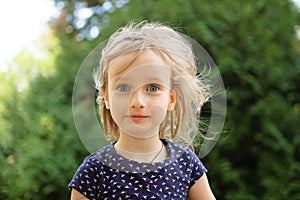 Closeup Portrait of Cute Little Blonde Girl Looking at the Camera Surprised During Summer Day in the Park. Happy Kid