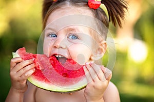 Closeup portrait of cute little girl eating watermelon on the grass in summertime