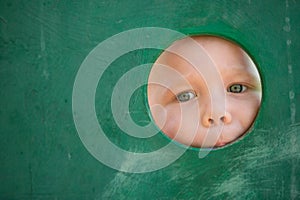 Closeup portrait of cute little toddler boy looking into green wooden frame at a playground. Curiosity, exploration and leaning.