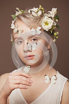 Closeup portrait of cute woman blonde model with healthy updo hairdo, white spring flowers and gentle butterfly on brown