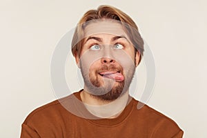 Closeup portrait of dumb fool bearded man looking cross-eyed and showing tongue out, fooling around