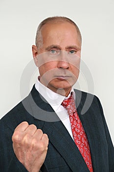 closeup portrait of elderly man in dark suit and red tie in style of Russian President Putin shows his fist against light photo