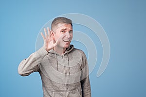 Closeup portrait of european man placing hand on ear listening carefully to gossip isolated on colored blue background