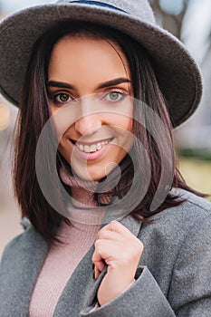 Closeup portrait fashionable charming young woman with brunette hair, in grey hat smiling to camera on street in city