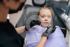 Closeup portrait of frightened cute little girl sitting in dental chair and looking at camera. Back view of female