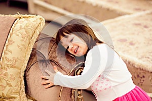 Closeup portrait of a funny little girl hugging sofa