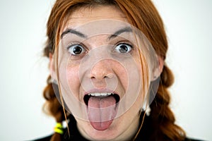 Closeup portrait of a funny redhead teenage girl with childish hairstyle sticking out her tongue isolated on white backround