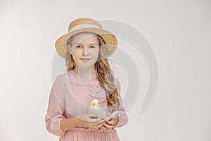 Closeup portrait of a girl in a straw hat with a toy bird in her hands with long blond hair on an  light