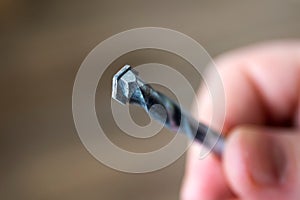 A closeup portrait of a hand of a person holding a stone drill bit. The high speed steel metal tool is spiral shaped and is used