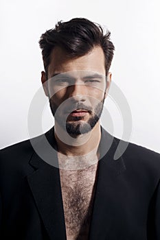 Closeup portrait of a handsome, brutal bearded man posing in black suit, with naked torso, isolated white background.