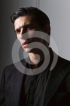 Closeup portrait of a handsome business man dressed in black suit against a dark grey background.