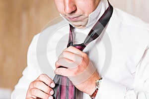 Closeup portrait of handsome businessman in suit putting on necktie indoors