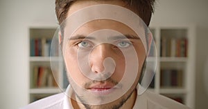 Closeup portrait of handsome caucasian male looking straight at camera in the library with bookshelves on the background