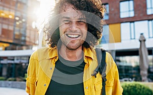 Closeup portrait of handsome happy man with curly hair smiling broadly, posing for social advertisement in the city street.