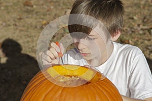 Closeup portrait of a young boy outside carving pumpkin