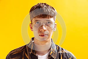 Closeup portrait of handsome young man, teen looking at camera isolated on bright yellow studio backgroud. Human