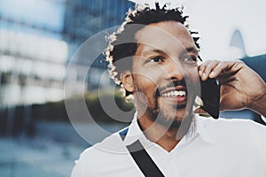 Closeup portrait of happy American African man using smartphone to call his friends at sunny city.Concept of happy young