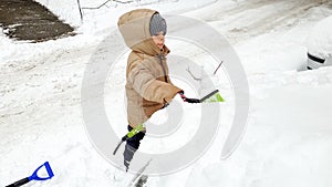 Closeup portrait of happy boy in jacket clean up snow covered car after snow storm using big brush . In the cold snowy