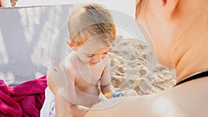 Closeup portrait of happy family adorable 3 years old toddler boy relaxing on beach and applying UV sun light protection