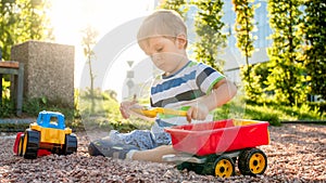 Closeup portrait of happy smiling 3 years old child boy digging sand on the playground with toy plastic truck or