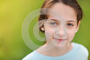 Closeup portrait of happy smiling little caucasian girl in earrings and blue blouse on warm green background